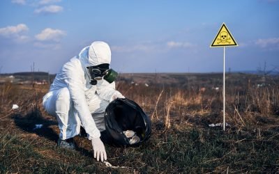 Male environmentalist in protective suit and gas mask putting trash into garbage bag with warning symbol of poisonous substances and danger. Concept of ecology, environmental pollution and hazard.