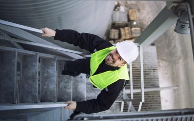 Top view of factory worker climbing metal stairs on industrial silo building.